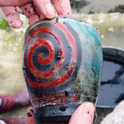 Raku pot with red and black spiral and turquoise crackle glaze held with two hands, only fingertips showing.